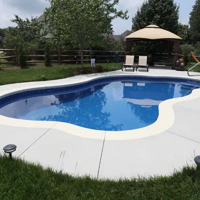 A modern rectangular pool with a stone paver deck and tropical landscaping.